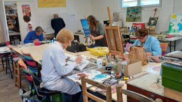 un homme et trois femmes assis autour d'une table d'atelier. ils sont en train de peindre.