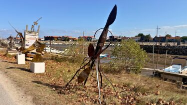 sculpture en acier représentant un animal marin dans l'herbe avec le port de La Teste en arrière-plan pour le festival Alias