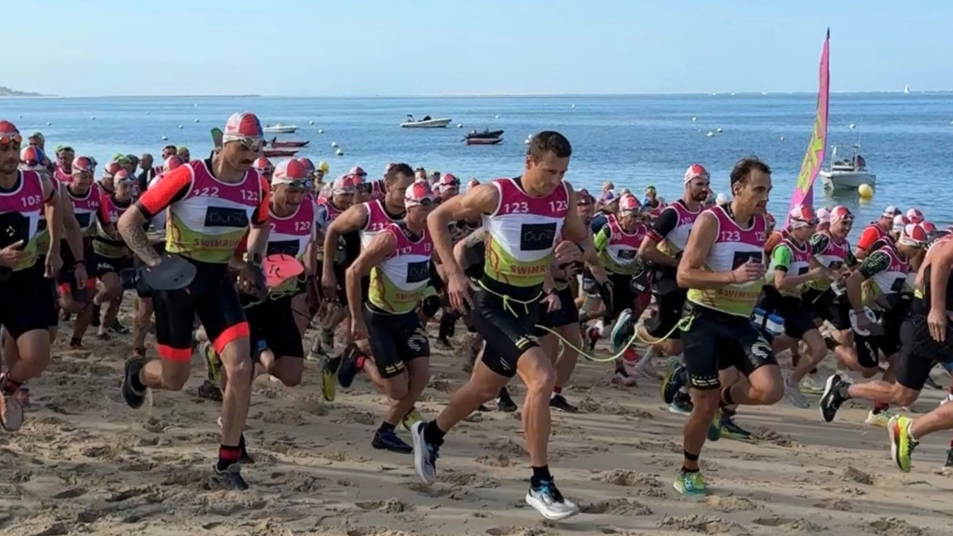 des sportifs en combi de plongée en train de courir sur la plage lors du swimrun du bassin d'arcachon