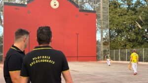 Deux coachs de l'équipe arcachonnaise de pelote basque observent de jeunes équipiers en train de s'entraîner face au fronton.