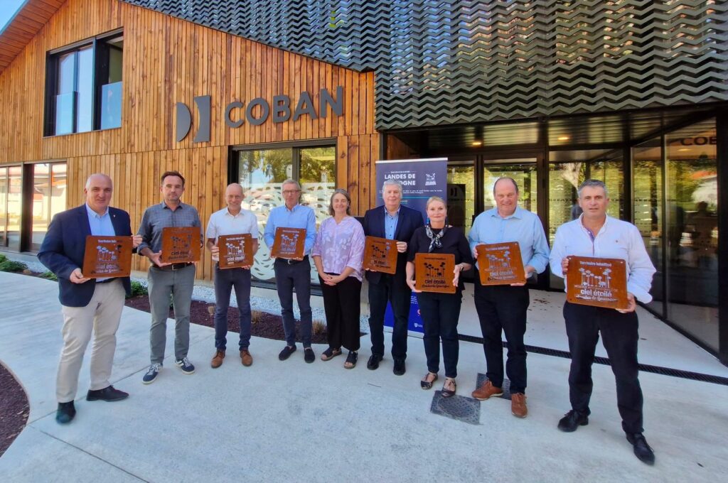 9 personnes debout devant un batiment en bois qui tiennent des plaques dans les mains