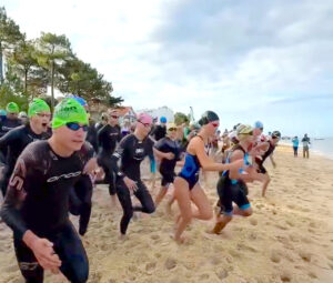 Des personnes en maillots de bains, combinaisons, lunettes de nage et bonnet s'élencent sur la ligne de départ d'une coruse sur une plage