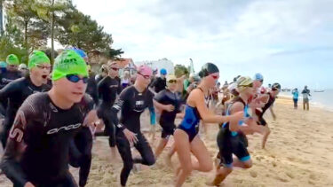 Des personnes en maillots de bains, combinaisons, lunettes de nage et bonnet s'élencent sur la ligne de départ d'une coruse sur une plage