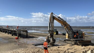 Un tractopelle sur la plage devant un bout de jetée sur le sable