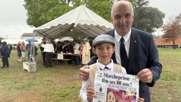 Un homme en costard et un enfant en tenu de gavroche se tiennt devant un stand surmonté d'une tente blanche. L'enfant tient une affiche : "80 ans de Marcheprime