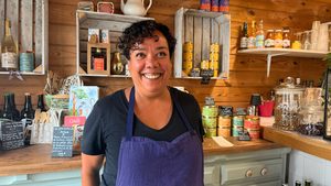 femme souriante qui porte un tablier devant un mur en bois avec des produits alimentaires exposés dans le restaurant