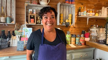 femme souriante qui porte un tablier devant un mur en bois avec des produits alimentaires exposés dans le restaurant
