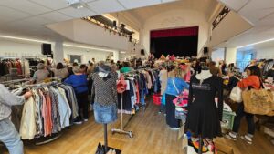 dans la salle publique du Teich, des rangées de portants avec des vêtements et des personnes qui participent à la braderie