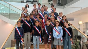 25 jeunes enfants et un adulte au milieu installés sur l'escalier de l'accueil de la mairie de la teste. Ils portent des écharpes tricolores.